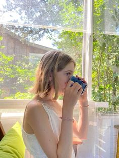 a young woman drinking from a cup in front of a window with the sun shining through