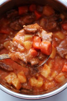 a ladle full of stew with meat and carrots in it, ready to be eaten