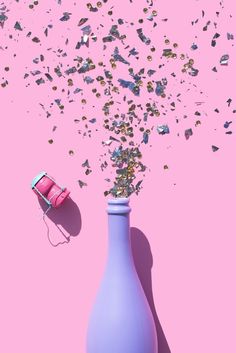 a purple vase with confetti spilling out of it on a pink surface next to a phone