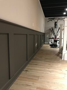 an empty room with hard wood flooring and gray paneling on the side wall