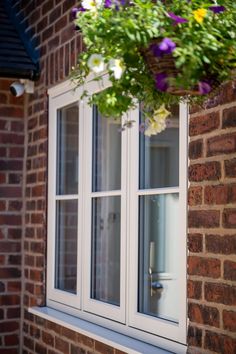 a window with flowers hanging from it's side and a brick building in the background