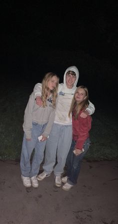 three people standing together in the dark with their arms around each other and one person wearing a hoodie