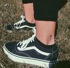 a cross tattoo on the ankle of a person wearing black and white shoes in grass