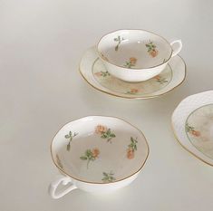 three teacups and saucers with flowers painted on the sides, sitting next to each other