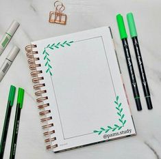 an open notebook with green markers and pencils next to it on a marble surface