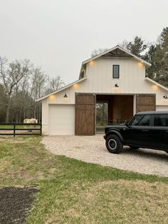 a black jeep is parked in front of a white barn with lights on the roof