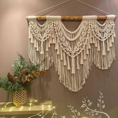 a macrame wall hanging on the wall next to a vase with pine cones