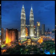 two tall buildings lit up at night in the middle of a city with skyscrapers