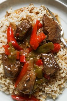 a white plate topped with rice covered in beef and peppers next to a fork on top of it