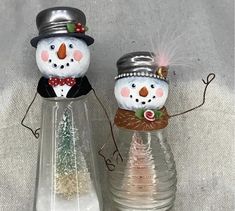 two snowmen standing next to each other in front of a glass vase with water