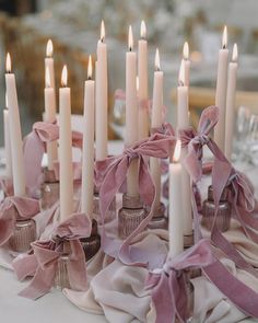 a table topped with lots of white candles covered in pink satin ribbons and bowknots