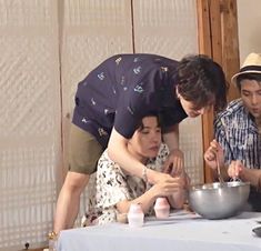 three people standing around a table with food on it and one person holding a bowl