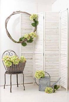 a room with white shutters and green flowers on the floor next to a chair