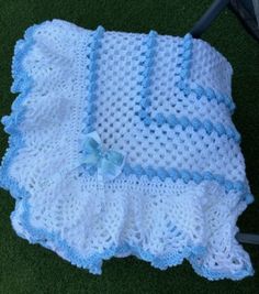 a crocheted blanket on the ground with a blue and white bow laying next to it