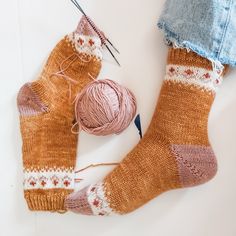 a pair of socks with yarn and knitting needles next to them on a white surface