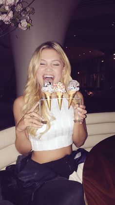 a woman sitting on top of a white couch holding up two desserts