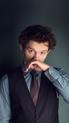 a young man in a suit and tie poses for a photo with his hands on his chin