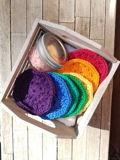 a wooden box filled with lots of different colored crocheted hats next to a mason jar