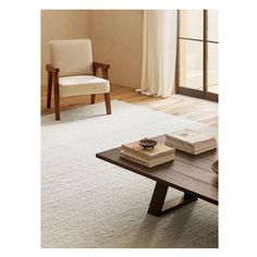 a coffee table with two books on it in front of a couch and chair next to a window