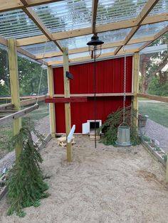 a red shed with a swing set and trees in the sand under it's roof