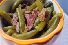 a bowl filled with green beans and ham on top of a table next to a napkin