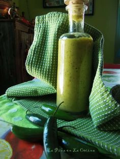 a bottle filled with green liquid sitting on top of a table next to some vegetables