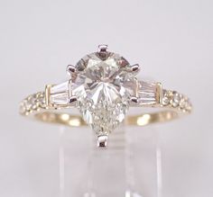 an engagement ring with a pear shaped diamond and baguettes on the sides, set in 18k yellow gold