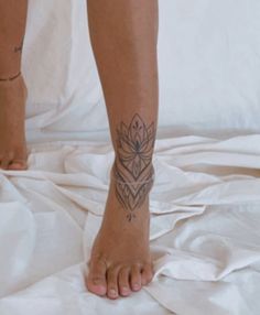 a person with a tattoo on their foot standing on a white sheeted bed spread