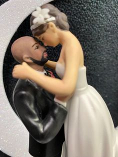 a bride and groom figurine kissing in front of a black background with white letters