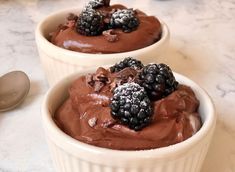 two white bowls filled with chocolate pudding and blackberries on top of a marble counter