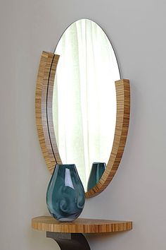 a round mirror sitting on top of a wooden shelf next to a vase with two blue glass vases