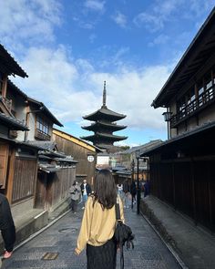 a woman walking down a street in front of tall buildings with pagodas on each side