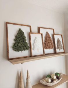 three framed christmas trees are hanging on the wall above a shelf with ornaments and other decorations