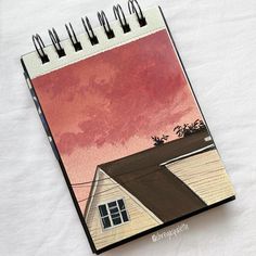 a spiral notebook with an image of a house on the front and red sky in the back