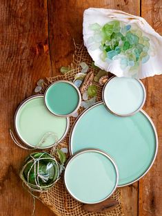 four different shades of green paint sitting on top of a wooden table next to a white flower