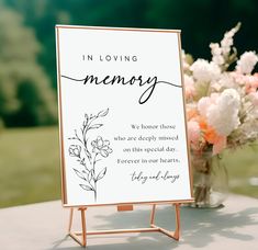 a sign that says in loving memory sitting on top of a table next to flowers