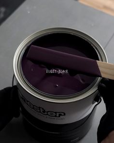 a person holding a paint brush over a can of violett - black acrylic