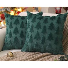 two green pillows sitting on top of a couch next to a christmas tree in the background