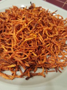 a white plate topped with fried carrots on top of a kitchen counter next to a red tile wall