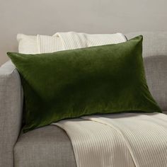 a green pillow sitting on top of a gray couch next to a white striped blanket