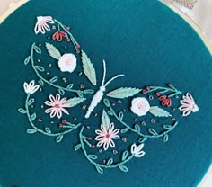 a close up of a embroidery pattern on a blue hoop with white flowers and green leaves