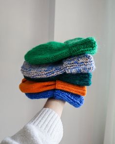 a person's hand holding four knitted mittens in different colors and sizes