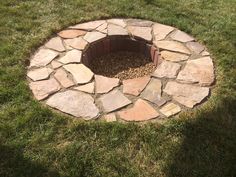 a stone fire pit in the middle of some grass