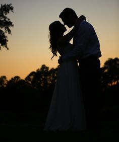 a bride and groom are silhouetted against the sunset