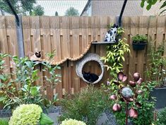 two cats are sitting on the top of a bird house in a garden with flowers and plants