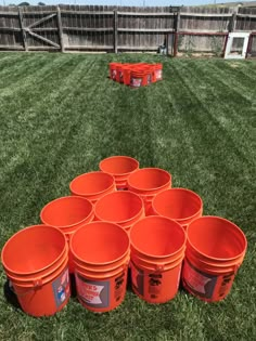 orange buckets sitting on the grass in front of an empty soccer field with red plastic containers