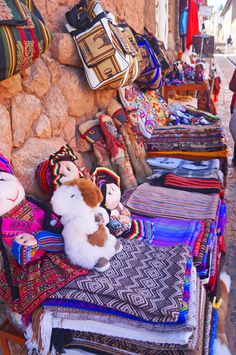 several stuffed animals are on display in front of bags and purses at an outdoor market