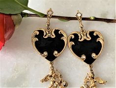 "Antique Gold Tone Hearts & Cupids Drop Pierced Earrings Black Enamel Hand Painted Hearts Hand Set with Faceted Crystal Stones Double Sided Cupids with Wings, Hearts and Bow & Arrows Dangle From the Enamel Hearts Cupids Hearts Hand Set with Faceted Crystal Stones Cupid Dangles are Double Sided with Crystals Hand Set on Both Sides of Hearts Each Earring Hand Set with 10 Crystals Earrings Measure 4 1/2\" Long Black Enamel Hearts Measure 1 1/4\" in Diameter Surgical Steel Posts Silver Tone Elegant Heart-shaped Enamel Earrings, Elegant Enamel Heart Earrings For Gift, Elegant Heart Enamel Earrings For Gift, Vintage Black Enamel Earrings For Gifts, Crystals Earrings, Painted Hearts, Bow Arrows, Crystal Stones, Earrings Black