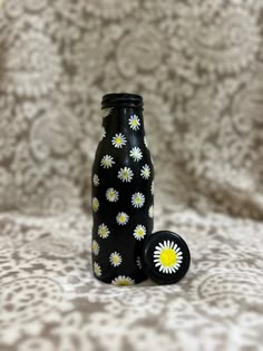 a black bottle with yellow and white daisies on it sitting on a tablecloth