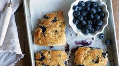 blueberry muffins are sitting on a baking sheet next to a bowl of berries